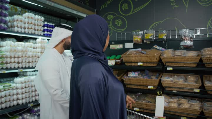 Buying cooking supplies and vegetables, wandering and shopping in the seasonal fruits and vegetables section in the Emirates, an Emirati Arab couple shopping at the supermarket, cooperation between family members in buying household needs, a local Emirati product