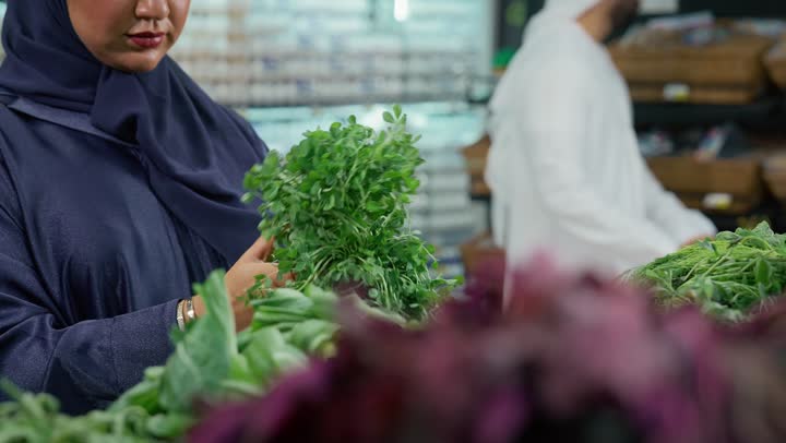 المحاصيل الزراعية الاماراتيه ذات الجودة العالية، انتقاء أجود أنواع الخضراوات الطازجة، امرأه عربيه خليجيه اماراتيه ترتدي عباءه رماديه تقوم ب انتقاء الخضار الطازج برفقه عائلتها، قسم الخضراوات في السوبر ماركت، توفيرالمنتجات للمستهلك ، محاصيل محليه