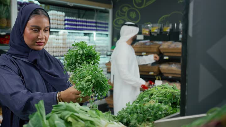 المحاصيل الزراعية الاماراتيه ذات الجودة العالية، انتقاء أجود أنواع الخضراوات الطازجة، امرأه عربيه خليجيه اماراتيه ترتدي عباءه رماديه تقوم ب انتقاء الخضار الطازج برفقه عائلتها، قسم الخضراوات في السوبر ماركت، توفيرالمنتجات للمستهلك ، محاصيل محليه