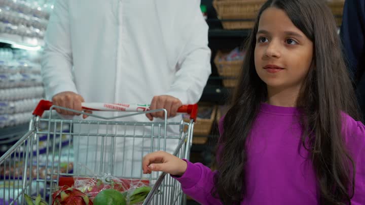 طفله اماراتيه تنتقي ثمره الرمان الطازج وتضعها في عربه التسوق،  السلع والمواد الغذائية المختلفة, رجل عربي اماراتي خليجي يرتدي الكندوره والغتره البيضاء يتبضع في قسم الخضراوات داخل السوبرماركت برفقه عائلته، شراء الاحتياجات المنزلية، منتجات ومحاصيل وطنيه