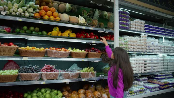 التأثير الإيجابي للتسوق مع العائلة، متعة التسوق والتبضع وشراء الإحتياجات المنزلية من السوبرماركت مع الأبناء، رجل عربي خليجي اماراتي يرتدي الكندوره والغتره البيضاء برفقة ابنته ويقوم بانتقاء ثمره الاناناس، قسم الفواكه الطازجة في متجر المواد الغذائية