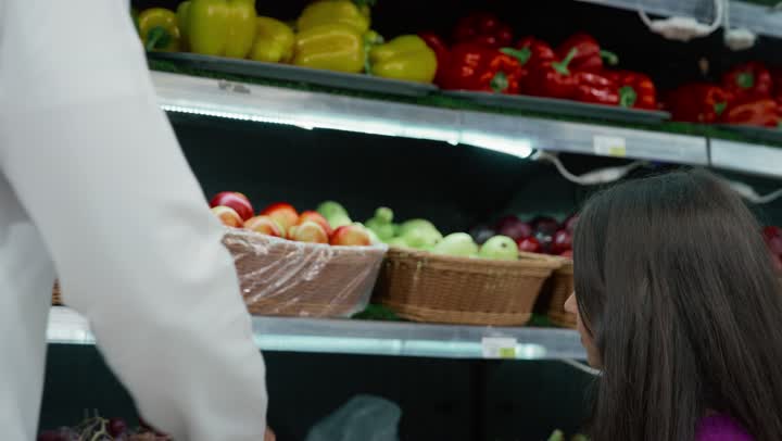 An Emirati Gulf Arab girl with her father, buying household needs inside the supermarket, an Emirati man giving his daughter an apple, consumer supplies, local national crops, fresh fruits and vegetables