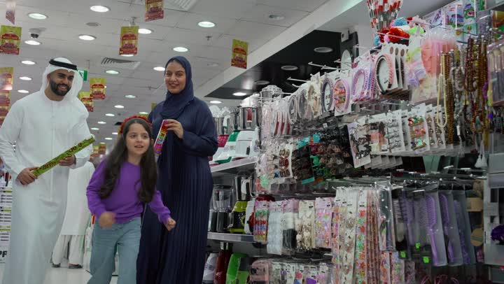 التمتع بالتخفيضات والعروض، فتاة عربية خليجية اماراتية تقوم بالركض والتجول في أحد أقسام السوبر ماركت برفقة أبيها وأمها بإيماءات السعادة والسرور، المشاركة والتعاون بين أفراد الأسرة, قضاء أوقات ممتعة بالتسوق واختيار اللوازم المنزليه.