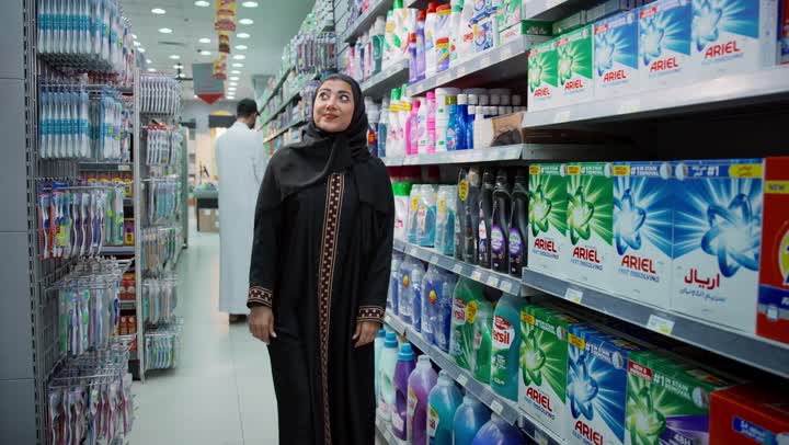 التجول في قسم المنظفات والمطهرات، امتلاك خيارات شراء و استهلاك مختلفة في السوبرماركت، سيدة عربيه خليجية إماراتية محجبة ترتدي العباءة تمشي في أحد أقسام المتجر بإيماءات السرور، قضاء وقت ممتع في اختيار اللوازم المنزليه, السهولة والراحة في التسوق