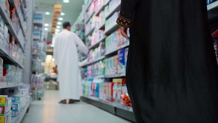 قضاء وقت ممتع في اختيار اللوازم المنزلية، التجول في قسم المنظفات والمطهرات، امتلاك خيارات شراء و استهلاك مختلفة في السوبرماركت، تصوير من الخلف لسيدة عربيه خليجية إماراتية محجبة ترتدي العباءة تمشي في أحد أقسام المتجر, السهولة والراحة في التسوق