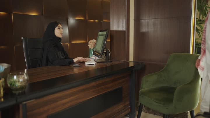 Receiving room card, using modern means and technologies in electronic payment, customer service in tourist hotels, inquiries and inquiries about hotel services, reservation procedures and entry to the reception desk, a Saudi Arabian Gulf woman wearing an abaya and hijab working in the field of inquiries
