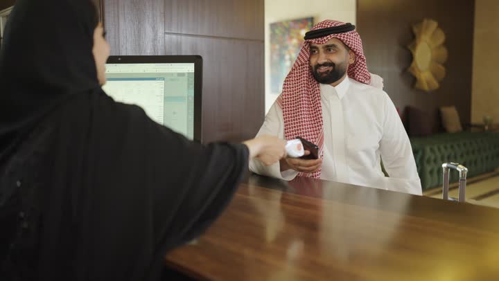 Inquiries and inquiries about hotel services, customer service in tourist hotels, reservation procedures and entry at the reception desk, a Saudi Arabian Gulf woman wearing an abaya and hijab working in the field of inquiries