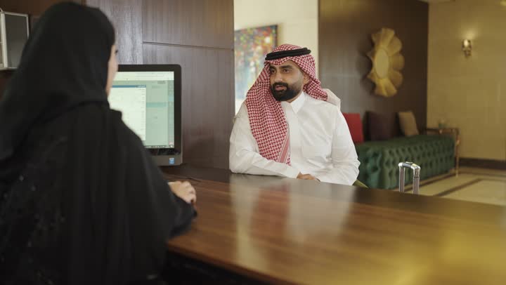 Booking and check-in procedures at the reception desk, customer service in tourist hotels, a Saudi Arabian Gulf woman wearing an abaya and hijab working in the information field, inquiries and questions about hotel services
