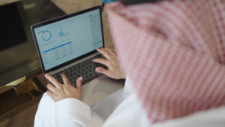 العمل عن بعد وتصفح الانترنت، أداء المهام والاعمال المكتبية،استخدام الأجهزة التقنية الحديثة و المتطورة , رجل عربي خليجي سعودي يجلس على الاريكة في غرفة فندقية، استخدام جهاز الحاسوب المحمول، انجاز مهام العمل، احتراف وظائف الحاسوب وتكنولوجيا المعلومات
