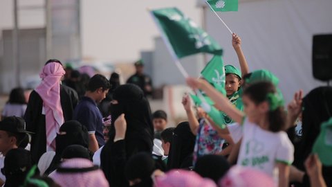 Raising the flags of the Kingdom of Saudi Arabia, the banner of monotheism and Islam and the slogan of national identity, Saudi citizens celebrating on the road, the concept of love of the homeland and belonging to it, loyalty and allegiance to the country, celebrating national occasions and holidays, the anniversary of the National Day on September 23, Flag Day on March 11