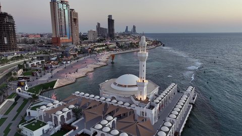 مسجد الرحمة العائم على البحر الأحمر في مدينة جدة في المملكة العربية السعودية، الفن الهندسي المعماري للابراج المطلة على ساحل الخليج العربي، الواجهه البحرية في النهار، تصوير درون جوي لكورنيش جدة السياحية