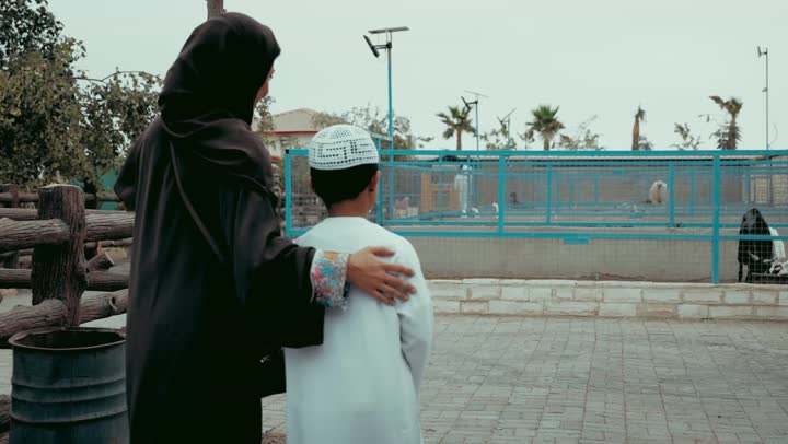 Having a good time watching animals, family entertainment concept, family visit to the zoo, entertaining and enjoyable tour among the open cages, an Arab Gulf Emirati woman wearing a black abaya points to the cage with her child