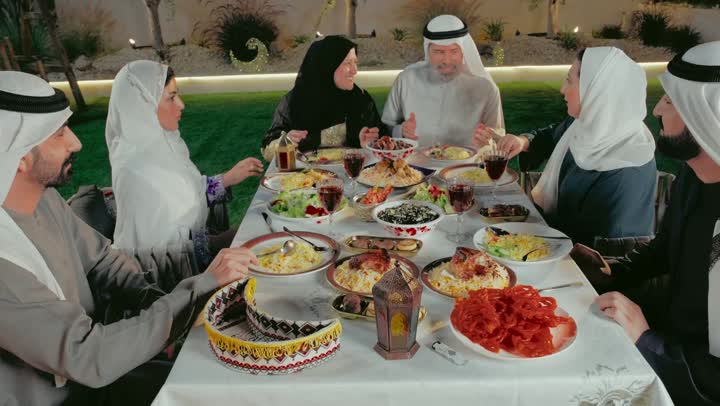 A happy Ramadan religious family atmosphere, an Arab Gulf Emirati family gathered around the dining table, a table filled with delicious oriental foods, performing the ritual of fasting in the holy month of Ramadan, exchanging conversations between family members, Islamic occasion decorations