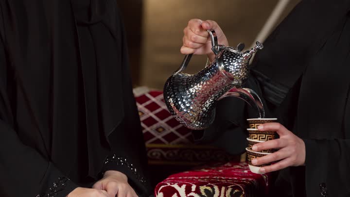 كرم الضيافة وحسن الاستقبال في شهر رمضان, زينة وإضاءة رمضانية، تقديم القهوة العربية الساخنة للضيف، كشتة بر وتخييم في صحراء الإمارات، حوار ونقاش بين الاصدقاء، سيدتان عربيتان اماراتيتان خليجيتان ترتديان العباءة تجلسان في خيمة شعبية