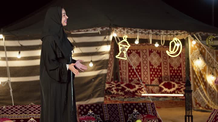 الترحيب والقاء التحية والسلام، قضاء وقت ممتع مع الأصدقاء، حسن استقبال الضيف, سيدتان عربيتان اماراتيتان خليجيتان ترتديان العباءة تتصافحان بحرارة بإيماءات السرور, زينة وإضاءة رمضانية, أجواء ليلية هادىْه في كشتة بر وتخييم في صحراء الإمارات