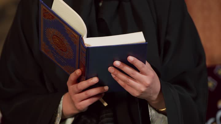 الاجتهاد في العبادة للتقرب إلى الله تعالى, الشعور بالخشوع والطمأنينة، قراءة السورالقصيرة والورد اليومي، تلاوة آيات من القرآن الكريم، كشتة بر وتخييم في صحراء الامارات،، تصوير مقرب لسيدة عربية خليجية إماراتية ترتدي عباءة تحمل بيدها المصحف الشريف وتقرأ منه