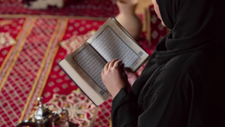 الاجتهاد في العبادة للتقرب إلى الله تعالى, الشعور بالخشوع والطمأنينة، قراءة السورالقصيرة والورد اليومي، تلاوة آيات من القرآن الكريم، كشتة بر وتخييم في صحراء الامارات،، تصوير مقرب لسيدة عربية خليجية إماراتية ترتدي عباءة تحمل بيدها المصحف الشريف وتقرأ منه