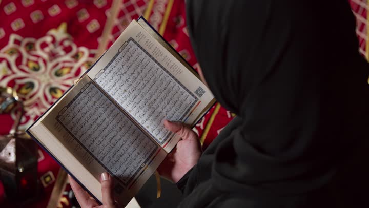 الاجتهاد في العبادة للتقرب إلى الله تعالى, الشعور بالخشوع والطمأنينة، قراءة السورالقصيرة والورد اليومي، تلاوة آيات من القرآن الكريم، كشتة بر وتخييم في صحراء الامارات،، تصوير مقرب لسيدة عربية خليجية إماراتية ترتدي عباءة تحمل بيدها المصحف الشريف وتقرأ منه