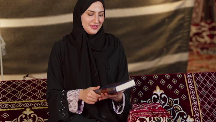 الشعور بالخشوع والطمأنينة، قراءة السورالقصيرة والورد اليومي، تلاوة آيات من القرآن الكريم، الاجتهاد في العبادة للتقرب إلى الله تعالى, كشتة بر وتخييم في صحراء الامارات، ديكور وزينة شهر رمضان، سيدة عربية خليجية إماراتية ترتدي عباءة تحمل بيدها المصحف الشريف وتقرأ منه