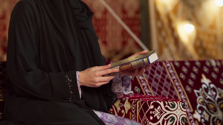 الشعور بالخشوع والطمأنينة، قراءة السورالقصيرة والورد اليومي، تلاوة آيات من القرآن الكريم، الاجتهاد في العبادة للتقرب إلى الله تعالى, كشتة بر وتخييم في صحراء الامارات، ديكور وزينة شهر رمضان، سيدة عربية خليجية إماراتية ترتدي عباءة تحمل بيدها المصحف الشريف وتقرأ منه