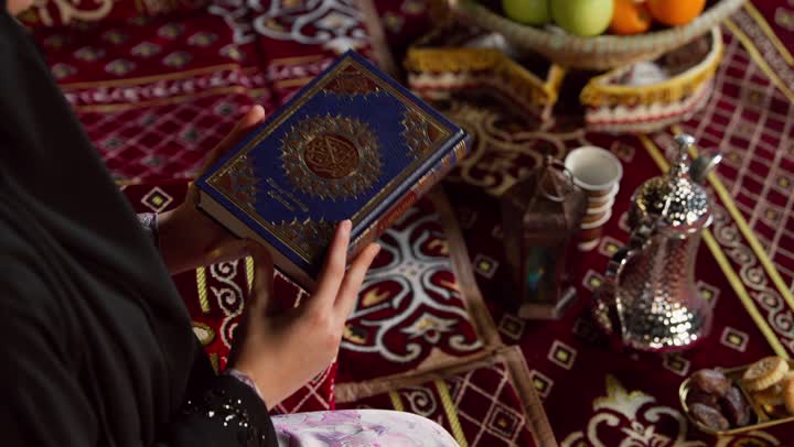 الاجتهاد في العبادة للتقرب إلى الله تعالى, الشعور بالخشوع والطمأنينة، قراءة السورالقصيرة والورد اليومي، تلاوة آيات من القرآن الكريم، كشتة بر وتخييم في صحراء الامارات،، تصوير مقرب لسيدة عربية خليجية إماراتية ترتدي عباءة تحمل بيدها المصحف الشريف وتقرأ منه