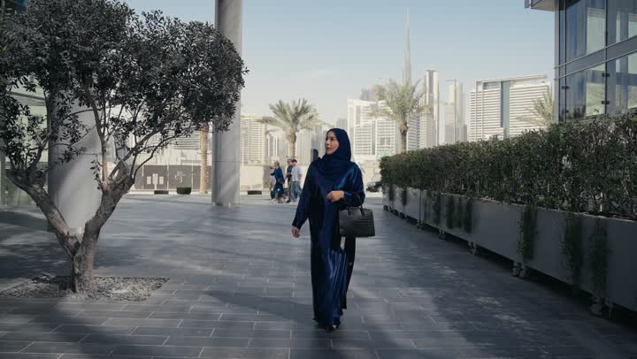 Attention to elegance and outward appearance, the concept of femininity and softness, a smiling Saudi Arabian Gulf woman wearing an abaya and hijab looking at something with gestures of pleasure and self-confidence, an Emirati woman wearing a colorful abaya and a black bag walking with confident steps