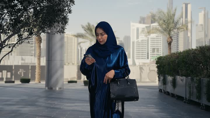 البحث عن شئ ما، امرأه عربيه خليجيه سعوديه تقوم بالنظر الي الهاتف المحمول،سيده اماراتيه ترتدي العباءه والحجاب تسير في احد الاماكن الخارجيه، ايماءه القلق والتوتر، اماكن ترفيهيه وسياحيه بالامارات العربيه المتحده