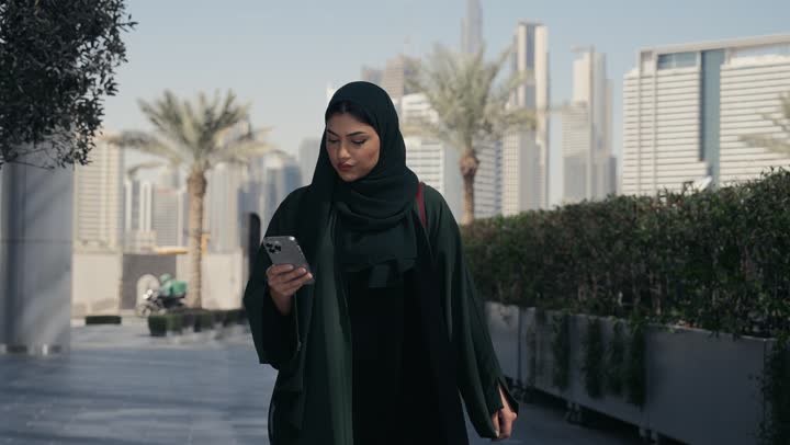 An Emirati Gulf Arab woman wearing an abaya and hijab walking in a shopping mall, a Saudi woman making a phone call, shopping places in the United Arab Emirates, interest in outward appearance, femininity and elegance