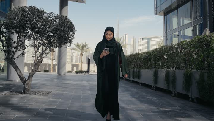سيده عربيه خليجيه اماراتيه ترتدي عباءه والحجاب تسير في احد اماكن التسوق، امرأه سعوديه تجري مكالمه هاتفيه، اماكن التسوق في الامارات العربيه المتحده، الاهتمام بالمظهرالخارجي، الانوثه والاناقه