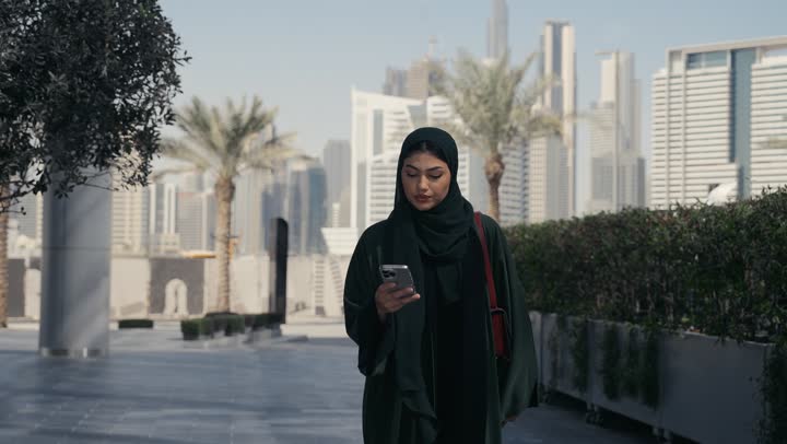 An Emirati Gulf Arab woman wearing an abaya and hijab walking in a shopping mall, a Saudi woman making a phone call, shopping places in the United Arab Emirates, interest in outward appearance, femininity and elegance