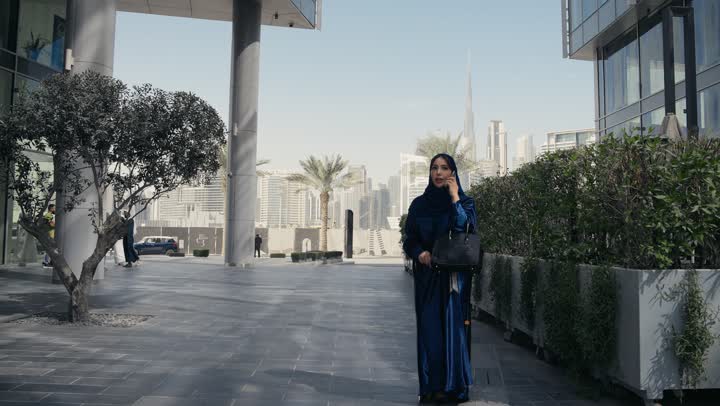 A Saudi Arabian Gulf woman hugs her friend with gestures of joy and smile, a Saudi woman wearing an abaya and hijab making a mobile phone call, gestures of hugging and love, spending fun times with friends, using modern technology