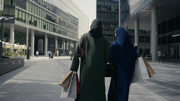 صديقتان اماراتيتان تحملان اكياس التسوق الملونه تسيران معاً في نزهة ممتعة لإحدى الأماكن الترفيهية، سيدتان خليجيتان سعوديتان ترتديان العباءة الخليجية تتحدثان عن السوالف، صداقات وتعارف، دردشة ومحادثات، قضاء وقت ممتع في الخارج