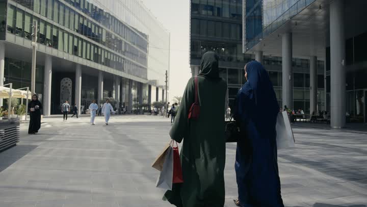 صديقتان اماراتيتان تحملان اكياس التسوق الملونه تسيران معاً في نزهة ممتعة لإحدى الأماكن الترفيهية، سيدتان خليجيتان سعوديتان ترتديان العباءة الخليجية تتحدثان عن السوالف، صداقات وتعارف، دردشة ومحادثات، قضاء وقت ممتع في الخارج