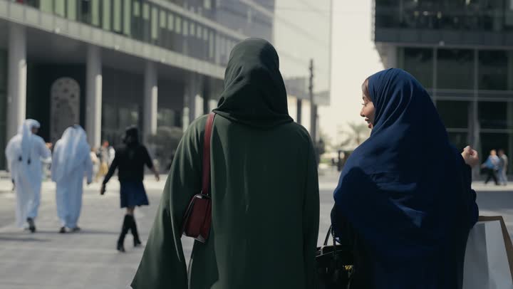 صديقتان اماراتيتان تحملان اكياس التسوق الملونه تسيران معاً في نزهة ممتعة لإحدى الأماكن الترفيهية، سيدتان خليجيتان سعوديتان ترتديان العباءة الخليجية تتحدثان عن السوالف، صداقات وتعارف، دردشة ومحادثات، قضاء وقت ممتع في الخارج