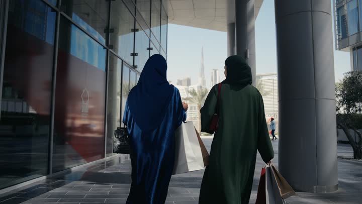 متعة مشاركة الأصدقاء في اختيار الهدايا من المراكز التجارية، الأثر الإيجابي للتسوق على النساء، إمرأتان عربيتان خليجيتان سعوديتان تحملان الأكياس الورقية تقومان بالتبضع، سيداتان اماراتيتان تتبادلان الاحاديث والاخبار، الاستفادة من حسومات الجمعة البيضاء