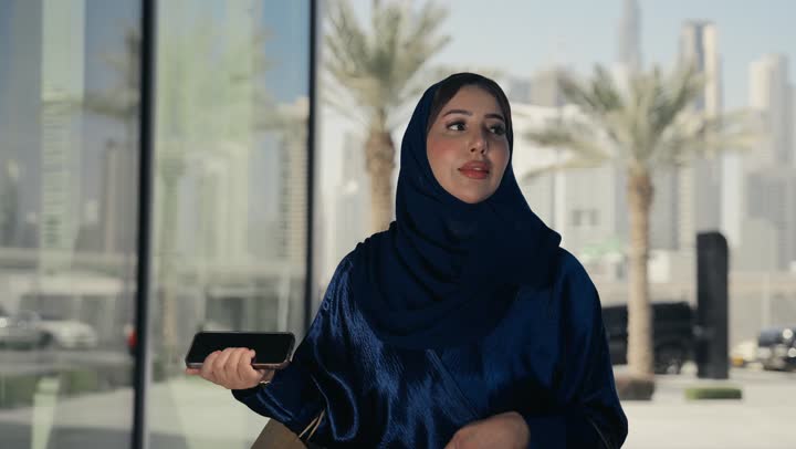 امراه عربيه خليجيه اماراتيه ترتدي عباءه ملونه تقوم بالنظر الي شئ ما، سيده سعوديه تسير فى احد الاماكن الخارجيه وتقوم بحمل كيس ورقي، التسوق وشراء الهدايا والمستلزمات، التمعن في شئ ما