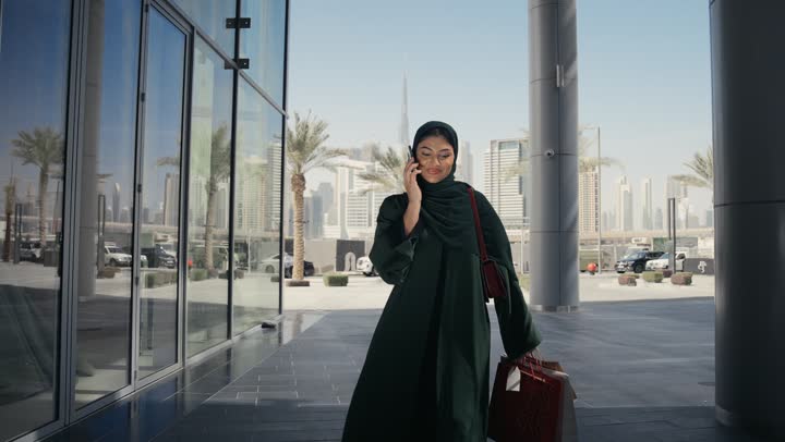مفهوم الأنوثة والنعومة, الاهتمام بالأناقة المظهر الخارجي, أزياء محجبات عصرية أنيقة, امرأة عربية خليجية سعودية محجبة ترتدي عباءة سوداء تقف امام متجر الألبسة، سيده اماراتيه تقوم بالتقاط صورلبعض الملابس النسائيه، التسوق والترفيه في الامارات المتحده
