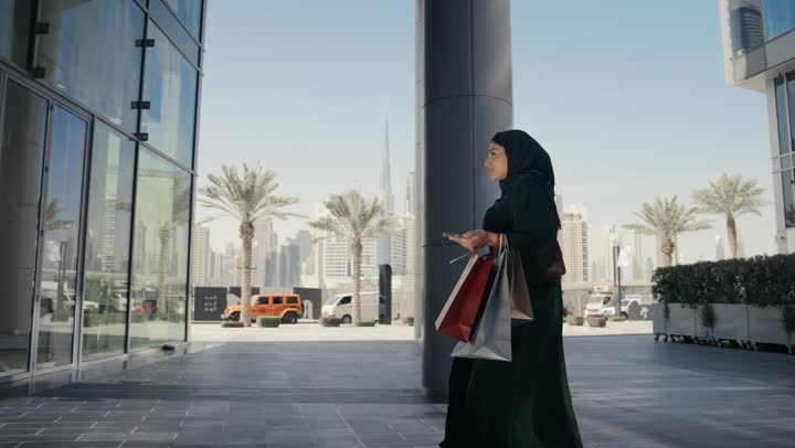 The concept of femininity and softness, interest in elegance and outward appearance, elegant modern veiled fashion, a veiled Saudi Arabian Gulf woman wearing a black abaya standing in front of a clothing store, an Emirati woman taking pictures of some women's clothing, shopping and entertainment in the United Arab Emirates