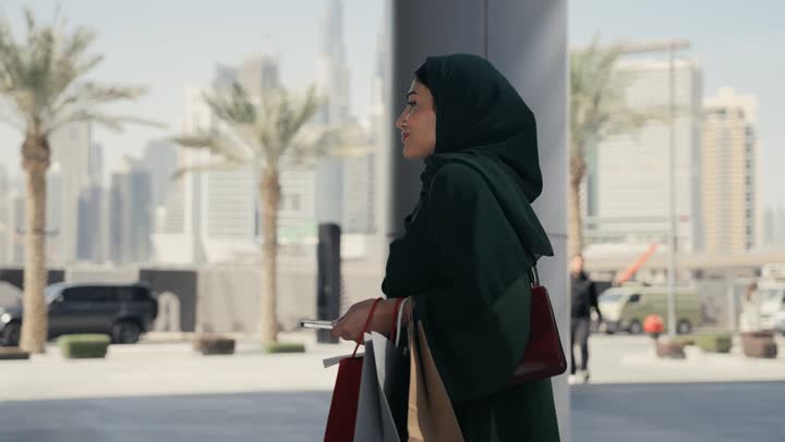 مفهوم الأنوثة والنعومة, الاهتمام بالأناقة المظهر الخارجي, أزياء محجبات عصرية أنيقة, امرأة عربية خليجية سعودية محجبة ترتدي عباءة سوداء تقف امام متجر الألبسة، سيده اماراتيه تقوم بالتقاط صورلبعض الملابس النسائيه، التسوق والترفيه في الامارات المتحده