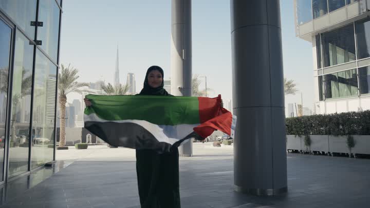 Showing feelings of pride in the homeland, national holidays and occasions, a veiled Emirati Gulf Arab woman wearing the UAE flag with a gesture indicating happiness, commemorating the National Day, the identity of the 51st UAE National Day, UAE Independence Day, love of the homeland, UAE National Day