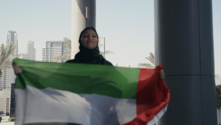 إظهار مشاعر الاعتزاز بالوطن، الأعياد والمناسبات الوطنية، سيدة عربية خليجية اماراتيه محجبة ترتدي علم الامارات بإيماء تدل على السعادة، إحياء ذكرى اليوم الوطني، هوية اليوم الوطني الإماراتي 51 ، يوم استقلال الإمارات، حب الوطن، العيد الوطني الإماراتي