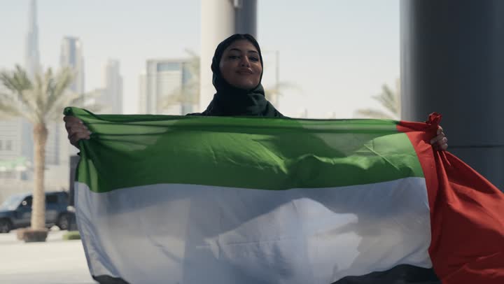 Showing feelings of pride in the homeland, national holidays and occasions, a veiled Emirati Gulf Arab woman wearing the UAE flag with a gesture indicating happiness, commemorating the National Day, the identity of the 51st UAE National Day, UAE Independence Day, love of the homeland, UAE National Day