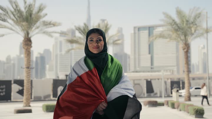امرأة عربية خليجية إماراتية تحمل علم الإمارات العربية المتحدة على ظهرها، الإحتفال باليوم الوطني الإماراتي، هوية اليوم الوطني الإماراتي 51، يوم استقلال الإمارات، العيد الوطني الإماراتي، الفخر والإعتزازبحب الوطن