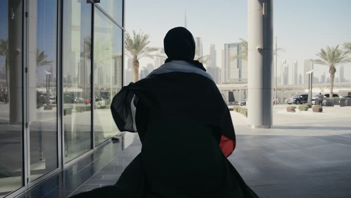 مفهوم حب الوطن والعلم، الإحتفال بالعيد الوطني الإماراتي 2 ديسمبر، إحياء ذكرى استقلال دولة الإمارات العربية المتحدة، امراة عربية خليجية إماراتية ترتدي عباءة سوداء تحمل علم الإمارات على ظهرها، الاعتزاز والفخر بإنجازات الوطن