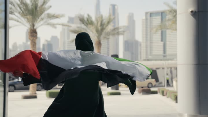 مفهوم حب الوطن والعلم، الإحتفال بالعيد الوطني الإماراتي 2 ديسمبر، إحياء ذكرى استقلال دولة الإمارات العربية المتحدة، امراة عربية خليجية إماراتية ترتدي عباءة سوداء تحمل علم الإمارات على ظهرها، الاعتزاز والفخر بإنجازات الوطن