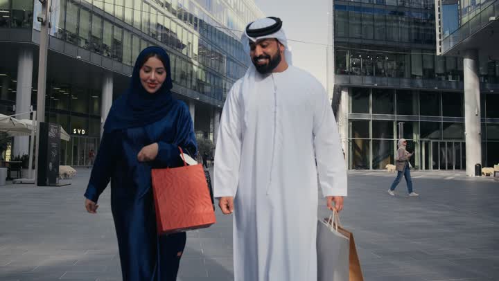 زوجان عربيان اماراتيان خليجيان سعيدان بالتسوق معا في المركز التجاري, سيدة جميلة وزوجها يحملان أكياس التسوق من المتجر, ماركات عالمية, التسوق في المول, متعة التسوق في الامارات العربيه المتحده
