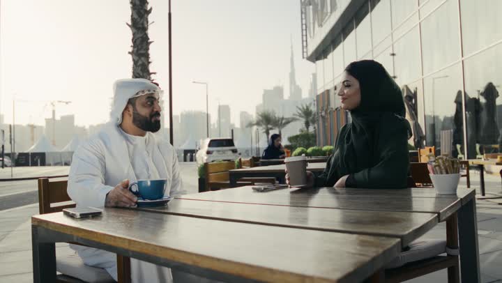 تناول القهوه الساخنه في الكافيهات الفاخرة، جلسة خارجية في الهواء الطلق للترويح عن النفس، تقوية الروابط الزوجية والعائلية، زوجان عربيان خليجيان اماراتيان يجلسان في احد المقاهي الخارجيه، التسامر والمناقشات، رجل اماراتي يستمتع باحتساء القهوه مع زوجته