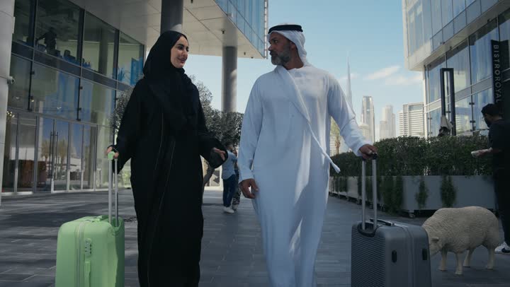 Spending a fun summer trip, the concept of tourism during summer vacation, an Arab Gulf Emirati couple dragging their luggage in front of the hotel, expressions and gestures of happiness and pleasure, a family having a good time, preparing to travel on a tourist tour