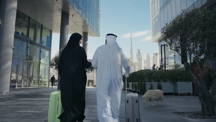 مفهوم السياحة في إجازة الصيف، تصوير من الخلف لزوجين عربيان خليجيين اماراتيين يجران حقائب الامتعة امام الفندق، عائلة سعودية تقضي وقت ممتع، الاستعداد للسفر في جولة سياحية، قضاء رحلة صيفية ممتعة ومسلية