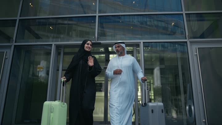 Spending a fun summer trip, the concept of tourism during summer vacation, an Arab Gulf Emirati couple dragging their luggage in front of the hotel, expressions and gestures of happiness and pleasure, a family having a good time, preparing to travel on a tourist tour